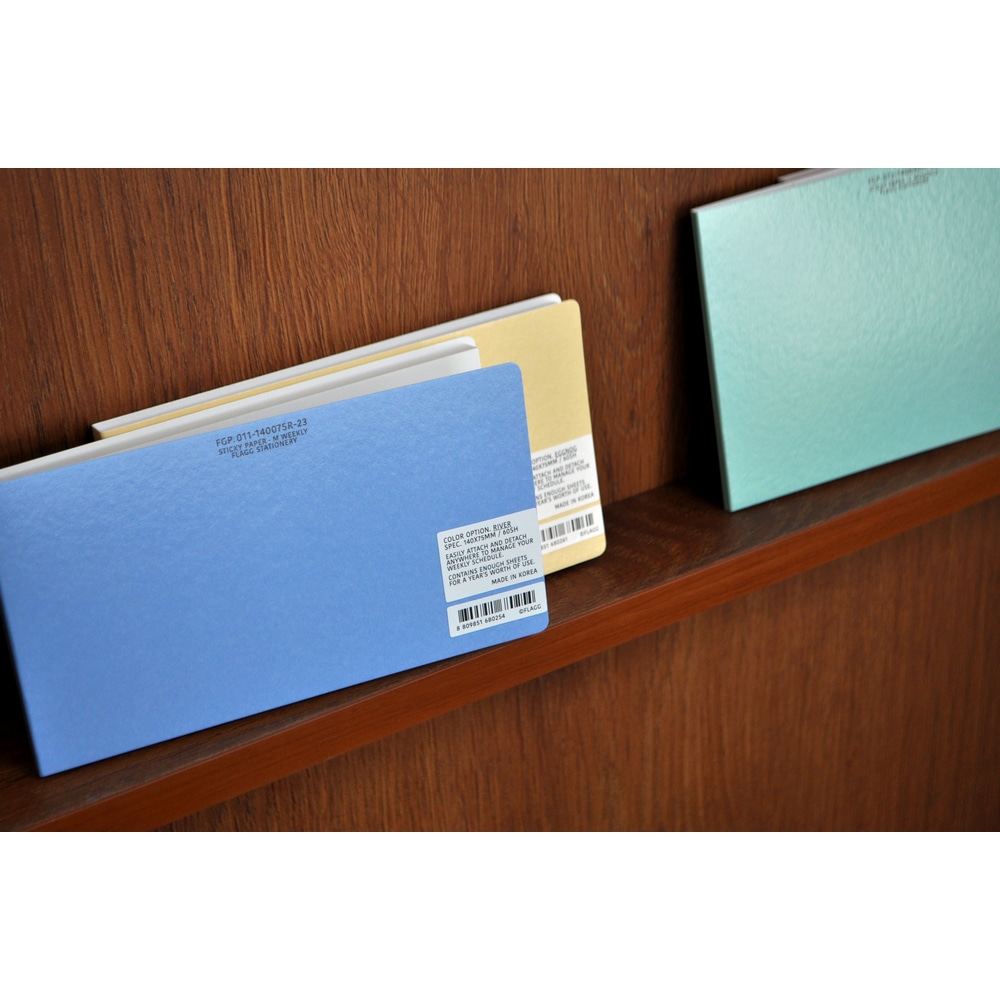 Die Stickypaper M in Blau und Gelb stehen in einem Holzdisplay. Daneben ist ein Stickypaper L mit M;onatsplaenen aufgestellt. 